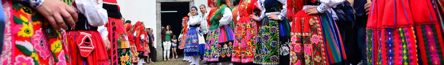 Na imagem vê-se a fachada da Capela de São João d'Arga com muitas raparigas vestidas com o traje regional de Lavradeira a ladear o caminho que dá acesso à capela